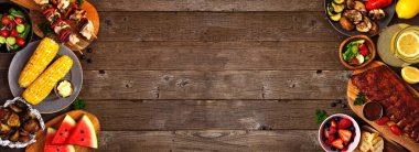 Yaz barbeküsü ya da piknik yemekleri. Kırsal bir ahşap pankartın üzerinde çifte sınır. Çeşitli ızgara etler, sebzeler, meyveler, salata ve patates. Kopyalama alanı ile görünümün üstünde.