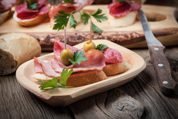 Tapas with sliced sausage, salami, olives and parsley. — Stock Photo, Image