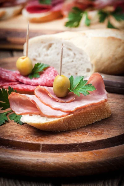 Tapas with sliced sausage, salami, olives and parsley. — Stock Photo, Image