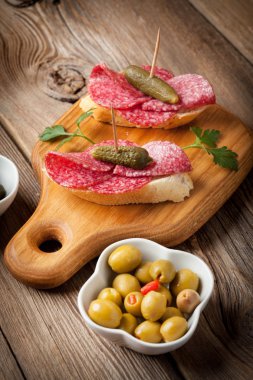 Dilimlenmiş salam, zeytin ve salatalığın üzerinde ahşap bir masa ile tapas.