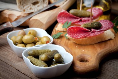 Dilimlenmiş salam, zeytin ve salatalığın üzerinde ahşap bir masa ile tapas.