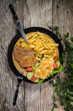 Kızarmış domuz pirzolası, patates kızartması ve salata ile servis edilir..