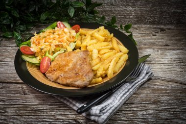 Kızarmış domuz pirzolası, patates kızartması ve salata ile servis edilir..