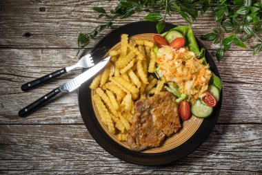 Kızarmış domuz pirzolası, patates kızartması ve salata ile servis edilir..