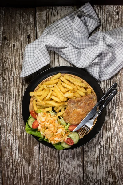 Fried pork chop in breadcrumbs, served with fries and salad. — Stock Photo, Image