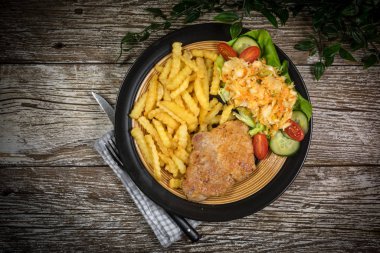Kızarmış domuz pirzolası, patates kızartması ve salata ile servis edilir..
