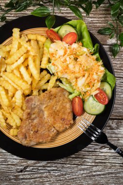 Kızarmış domuz pirzolası, patates kızartması ve salata ile servis edilir..