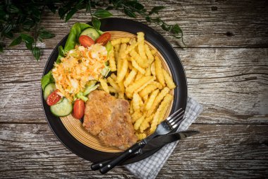 Kızarmış domuz pirzolası, patates kızartması ve salata ile servis edilir..