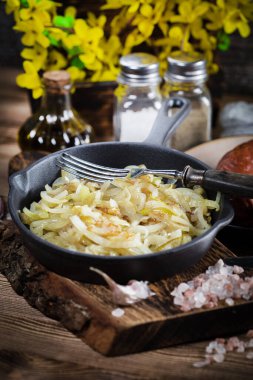 Tahta bir tezgahta duran dökme demir bir tavada kızarmış soğan..