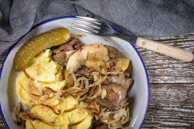 Kızarmış ciğer, soğan ve elma haşlanmış patates ve salatalık turşusu ile servis edilir. Üst görünüm.