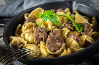 İtalyan makarna kabukları ve biftek sosu ahşap masada dökme demir tavada..