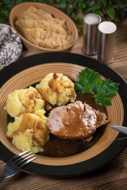 Kendi sosunda haşlanmış patates ve kızarmış lahanayla servis edilen haşlanmış domuz boynu. Sığ alan derinliği.