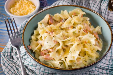 Tagliatelle Carbonara 'yı ahşap masada kasede yosunluyor. Sığ alan derinliği.