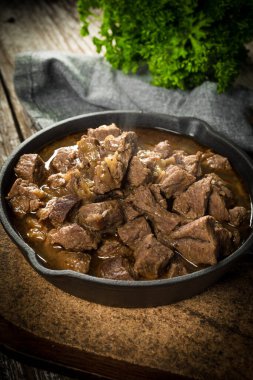 Dökme demir tavada sığır güveci, ahşap arka plan. Sığ alan derinliği.