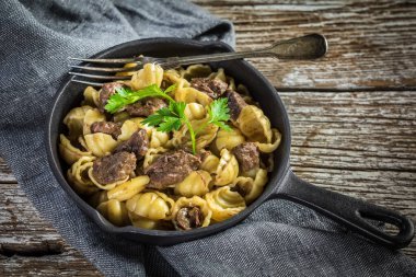 İtalyan makarna kabukları ve biftek sosu ahşap masada dökme demir tavada..