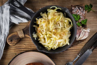 Tahta bir tezgahta duran dökme demir bir tavada kızarmış soğan..