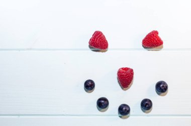 Ahududu ve yaban mersini soluk mavi ahşap arka planda sıralanmış gülen yüzler halinde. Taze organik sağlıklı diyet konsepti