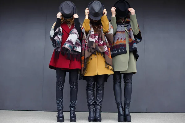 Chicas con estilo en abrigos de cachemira de moda de verde, amarillo y rojo, gafas negras, bufanda, y zapatos de cuero en el fondo de una pared gris — Foto de Stock