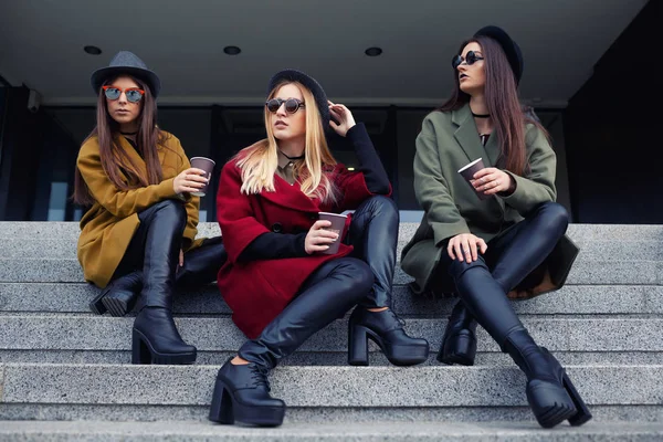 Şık kız trendy kat, eşarplar, şapka ve deri ayakkabı mutfak için merdivenlerde alışılmadık makyaj ile kahve içmek