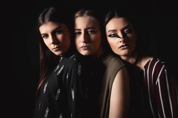 Три стильные модели с необычным макияжем и чертами лица на темном фоне — стоковое фото