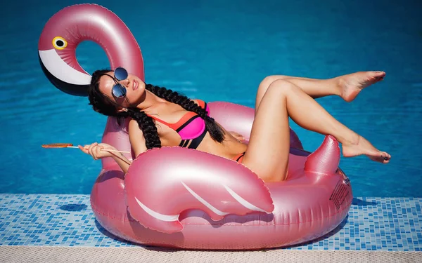 Havuzun arka plan üzerinde büyük bir karamel ile parlak bir mayo güzel bir saç kesimi ile güzel bir esmer bir flamingo üzerinde oturur