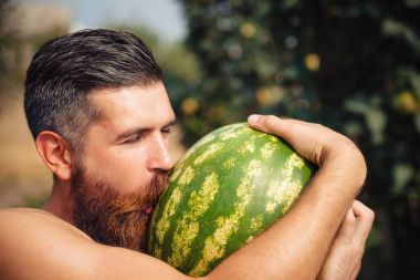 Bir adamla şık bir saç modeli, uzun sakalı karpuz öper.