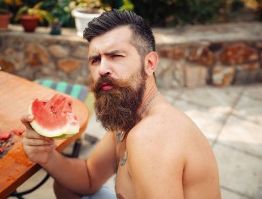 Bir adam şık bir saç modeli, uzun sakallı ve büyük bir zevk ile dövme karpuz yiyor