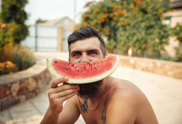 Bir adam şık bir saç modeli, uzun sakallı ve büyük bir zevk ile dövme karpuz yiyor