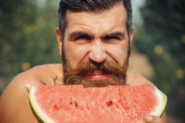 Bir adam şık bir saç modeli, uzun sakallı ve büyük bir zevk ile dövme karpuz yiyor
