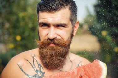Bir adam şık bir saç modeli, uzun sakallı ve büyük bir zevk ile dövme karpuz yiyor