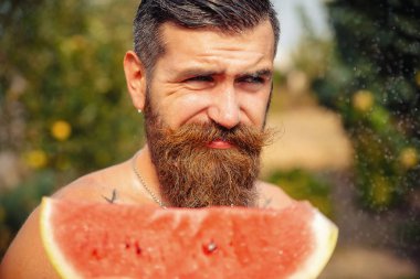 Bir adam şık bir saç modeli, uzun sakallı ve büyük bir zevk ile dövme karpuz yiyor