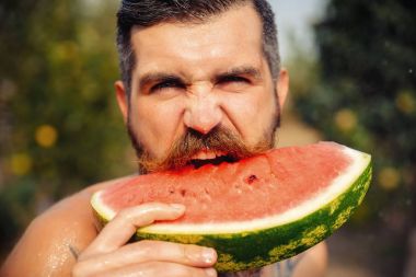 Bir adam şık bir saç modeli, uzun sakallı ve büyük bir zevk ile dövme karpuz yiyor
