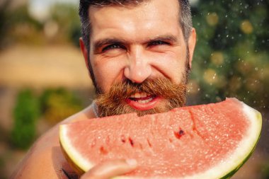 Bir adam şık bir saç modeli, uzun sakallı ve büyük bir zevk ile dövme karpuz yiyor