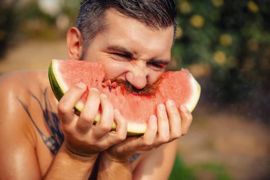 Bir adam şık bir saç modeli, uzun sakallı ve büyük bir zevk ile dövme karpuz yiyor