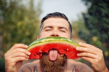 Bir adam şık bir saç modeli, uzun sakallı ve büyük bir zevk ile dövme karpuz yiyor