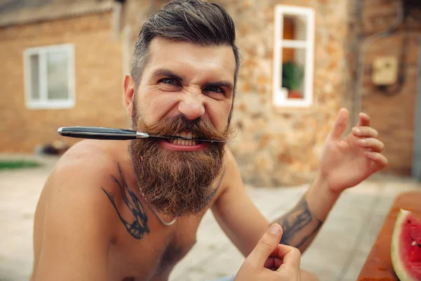 Bir adam şık bir saç modeli, uzun sakallı ve büyük bir zevk ile dövme karpuz yiyor