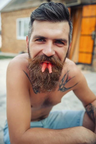 Bir adam şık bir saç modeli, uzun sakallı ve büyük bir zevk ile dövme karpuz yiyor