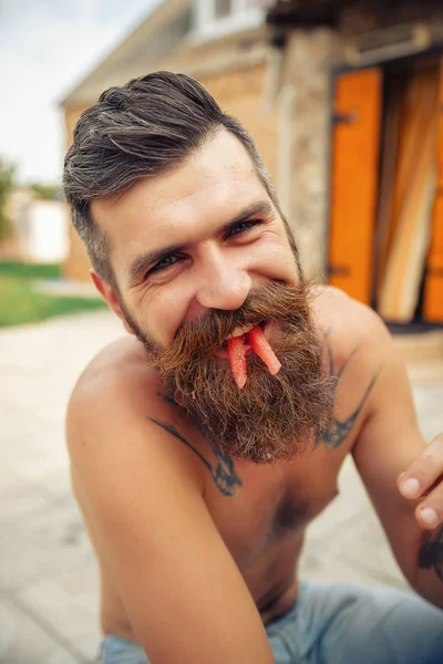 Bir adam şık bir saç modeli, uzun sakallı ve büyük bir zevk ile dövme karpuz yiyor