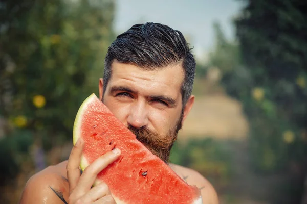 Bir adam şık bir saç modeli, uzun sakallı ve büyük bir zevk ile dövme karpuz yiyor