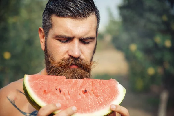Bir adam şık bir saç modeli, uzun sakallı ve büyük bir zevk ile dövme karpuz yiyor
