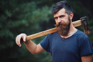 Siyah tişörtlü şık sakallı adam, kafasında kafasıyla ormanda tahta bir balta tutuyor.