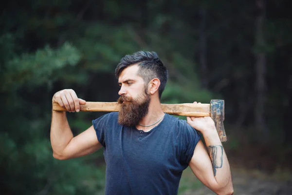 Stylish bearded man in a dark T-shirt, with a head on his head holding in his hands a wooden ax in the woods — Stock Photo, Image