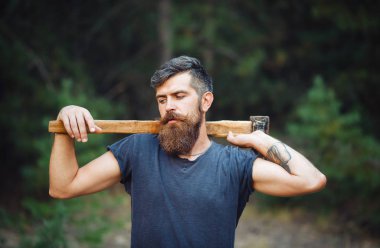 Siyah tişörtlü şık sakallı adam, kafasında kafasıyla ormanda tahta bir balta tutuyor.