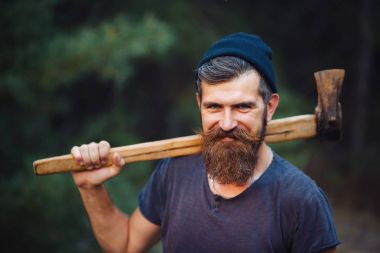 Siyah tişörtlü şık sakallı adam, kafasında kafasıyla ormanda tahta bir balta tutuyor.