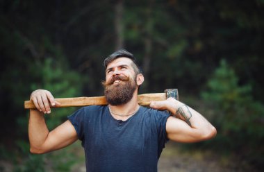 Siyah tişörtlü şık sakallı adam, kafasında kafasıyla ormanda tahta bir balta tutuyor.