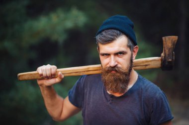 Siyah tişörtlü şık sakallı adam, kafasında kafasıyla ormanda tahta bir balta tutuyor.