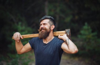 Siyah tişörtlü şık sakallı adam, kafasında kafasıyla ormanda tahta bir balta tutuyor.