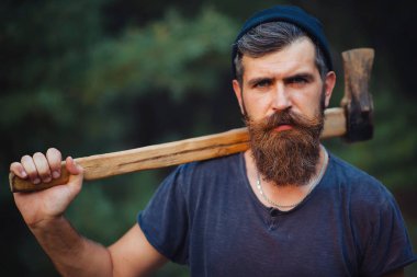 Siyah tişörtlü şık sakallı adam, kafasında kafasıyla ormanda tahta bir balta tutuyor.