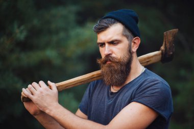 Siyah tişörtlü şık sakallı adam, kafasında kafasıyla ormanda tahta bir balta tutuyor.