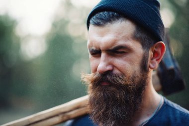 Siyah tişörtlü şık sakallı adam, kafasında kafasıyla ormanda tahta bir balta tutuyor.